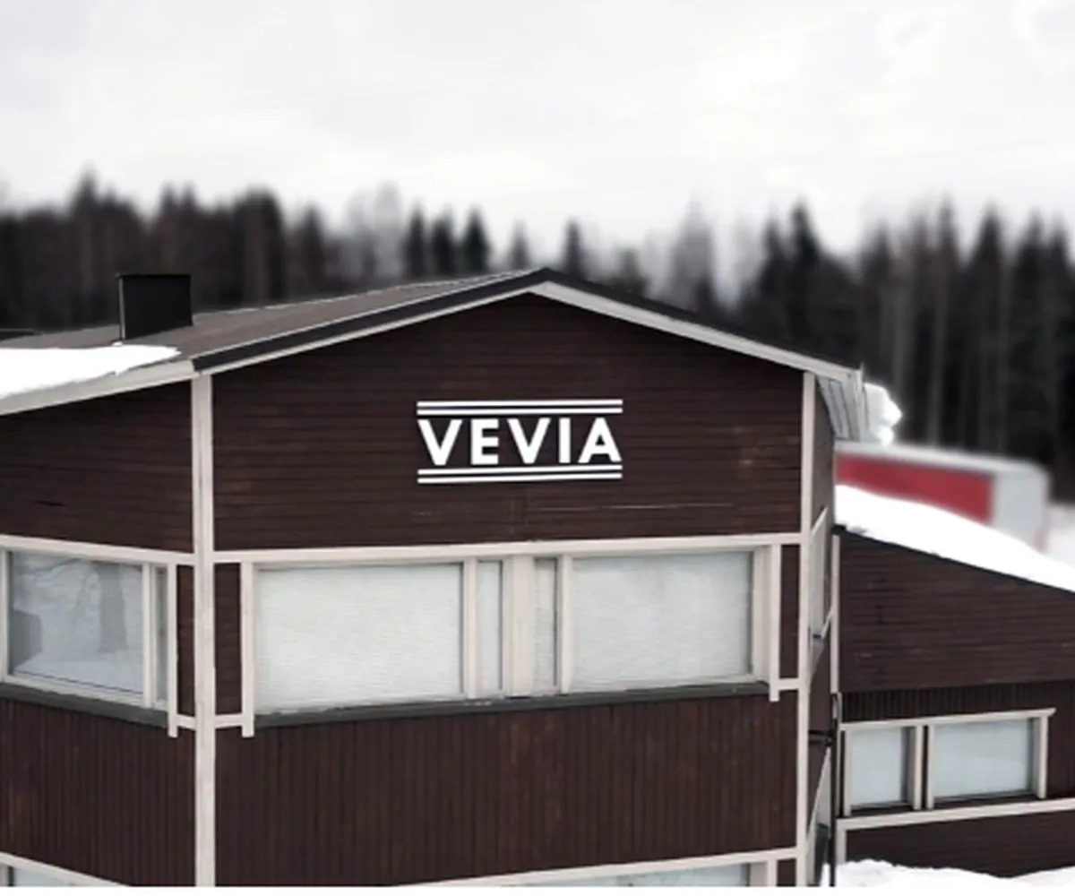 Vevian tummanruskea tehdasrakennus talvella, seinässä VEVIA-kyltti